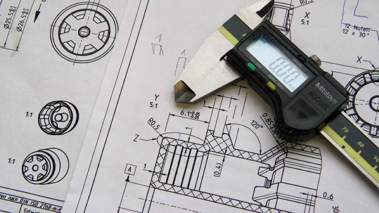 Digital calipers rest on a detailed mechanical engineering drawing.
