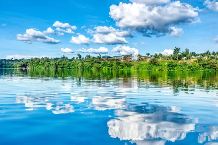 Wide view of the Nile River at Jinja, Uganda, with green banks and lakeside settlements under a blue sky.