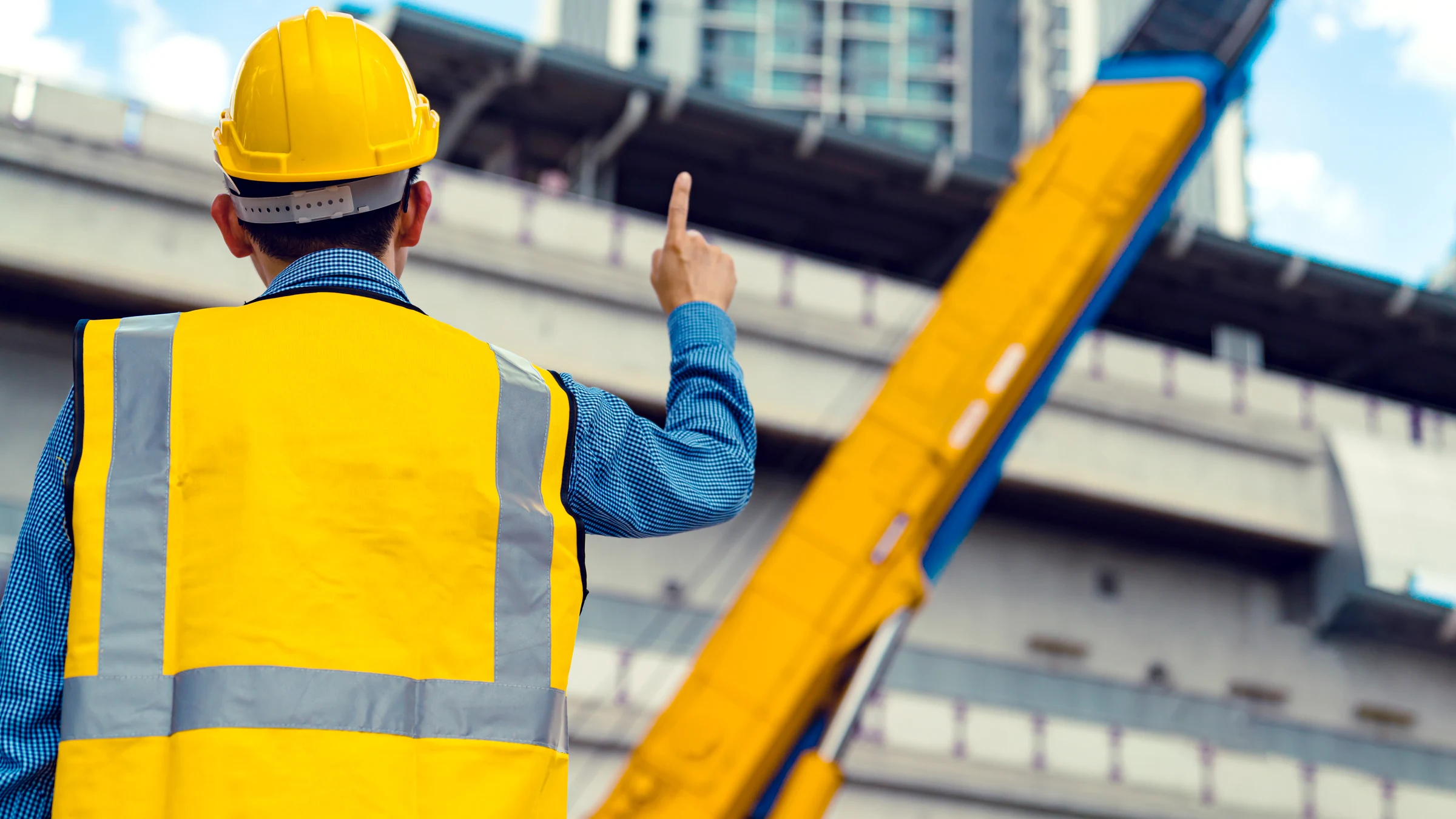 Engineer in a yellow safety vest and hard hat inspecting elevated infrastructure at a construction site.