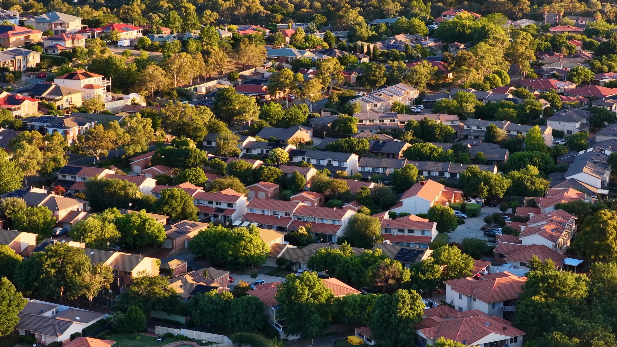 Aerial view of suburban houses, streets and mature trees in Canberra, Australia.