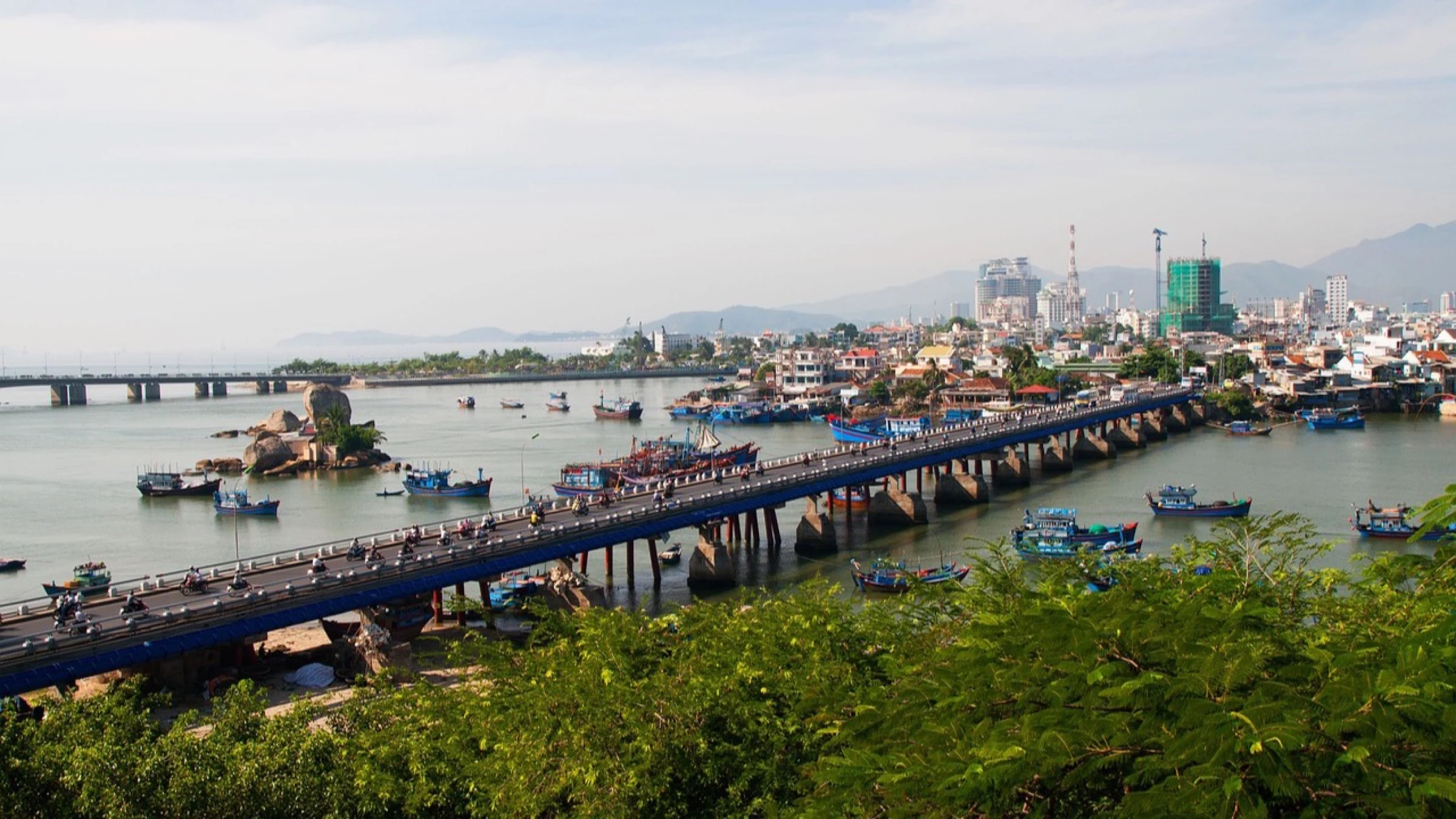 Boats on a river beside a bridge and port infrastructure in Viet Nam.