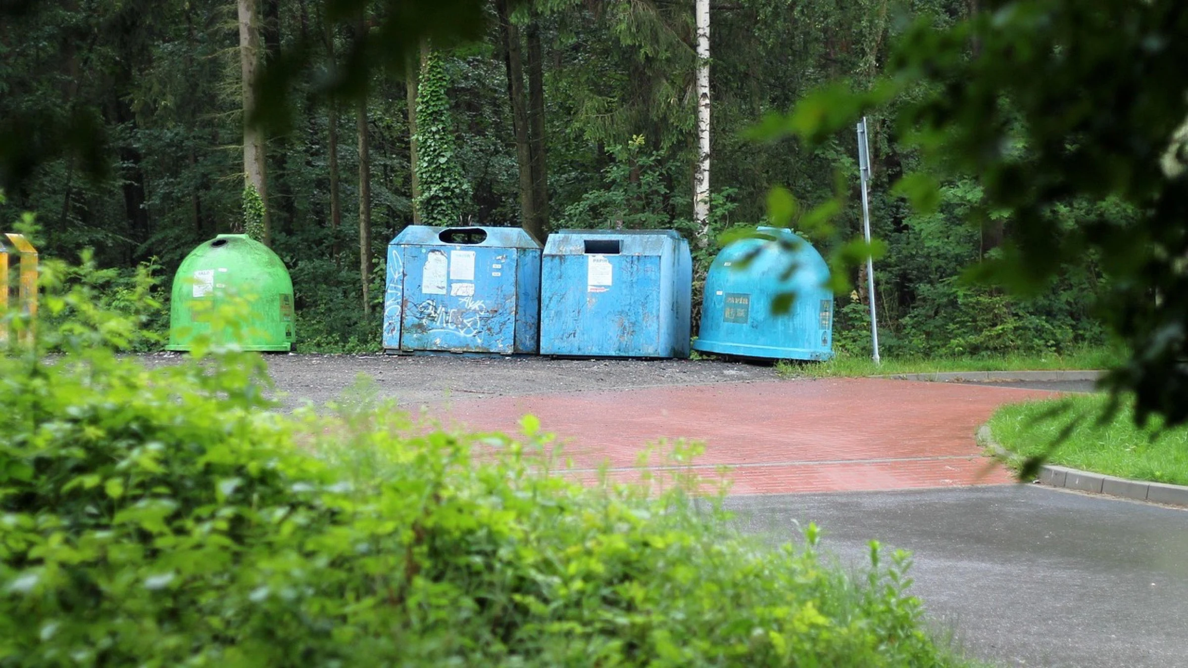Separate recycling containers beside a wooded road.
