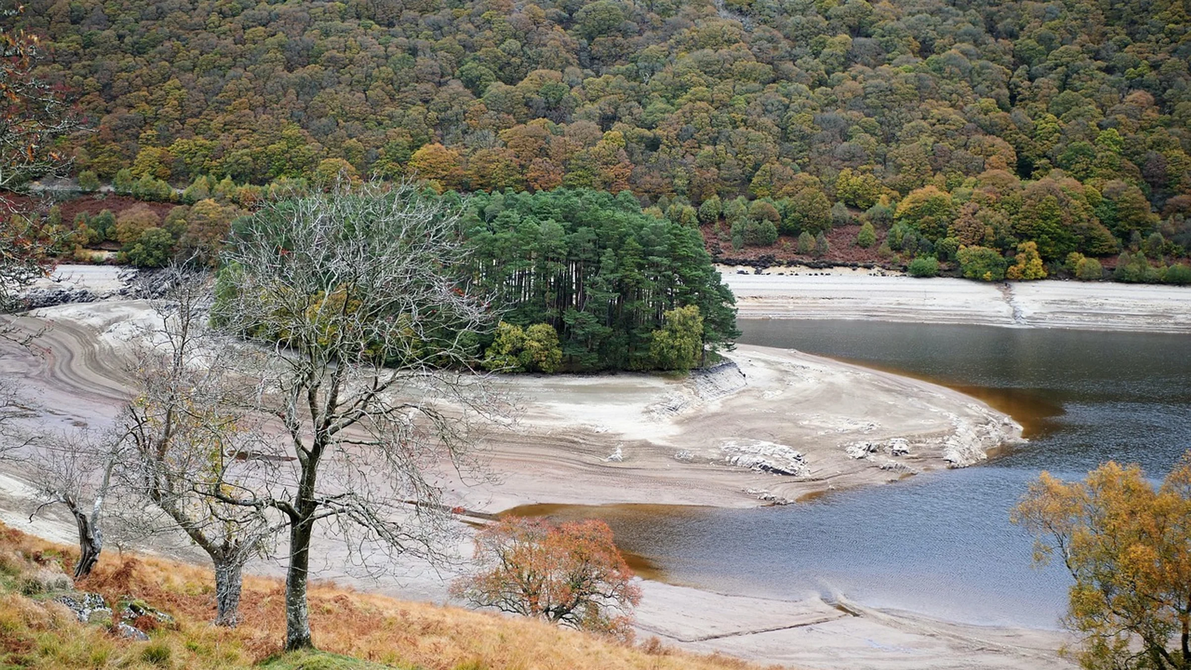 Low water exposes the banks of a reservoir beneath dry hills.