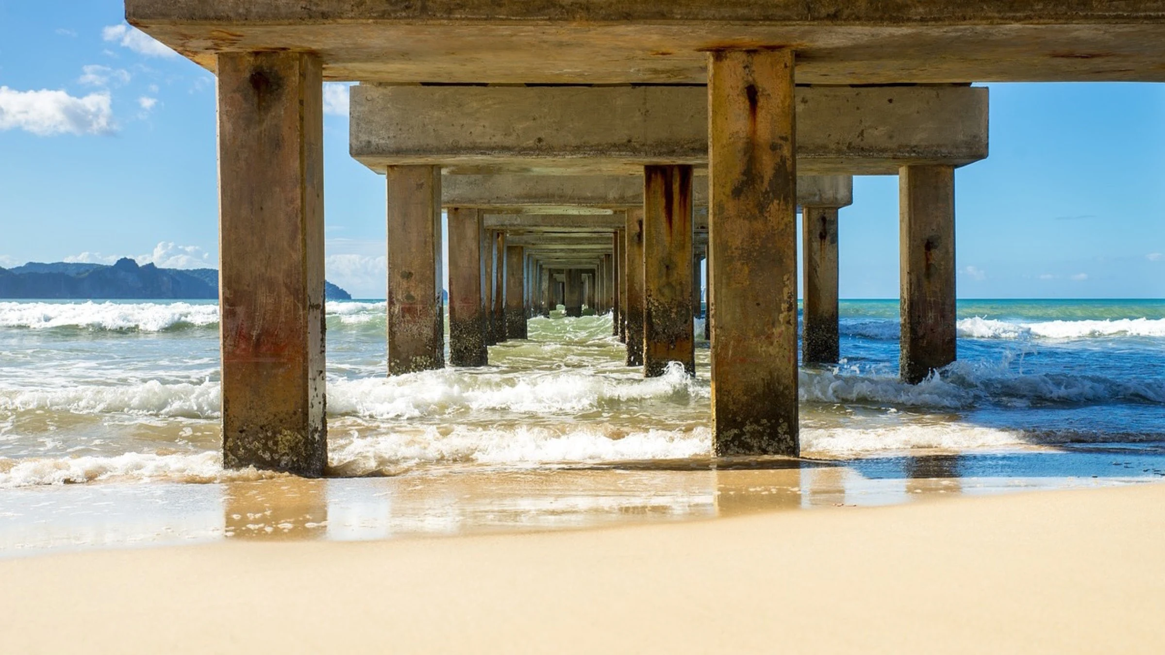 Concrete bridge columns extend from a sandy Philippine beach into shallow blue water.