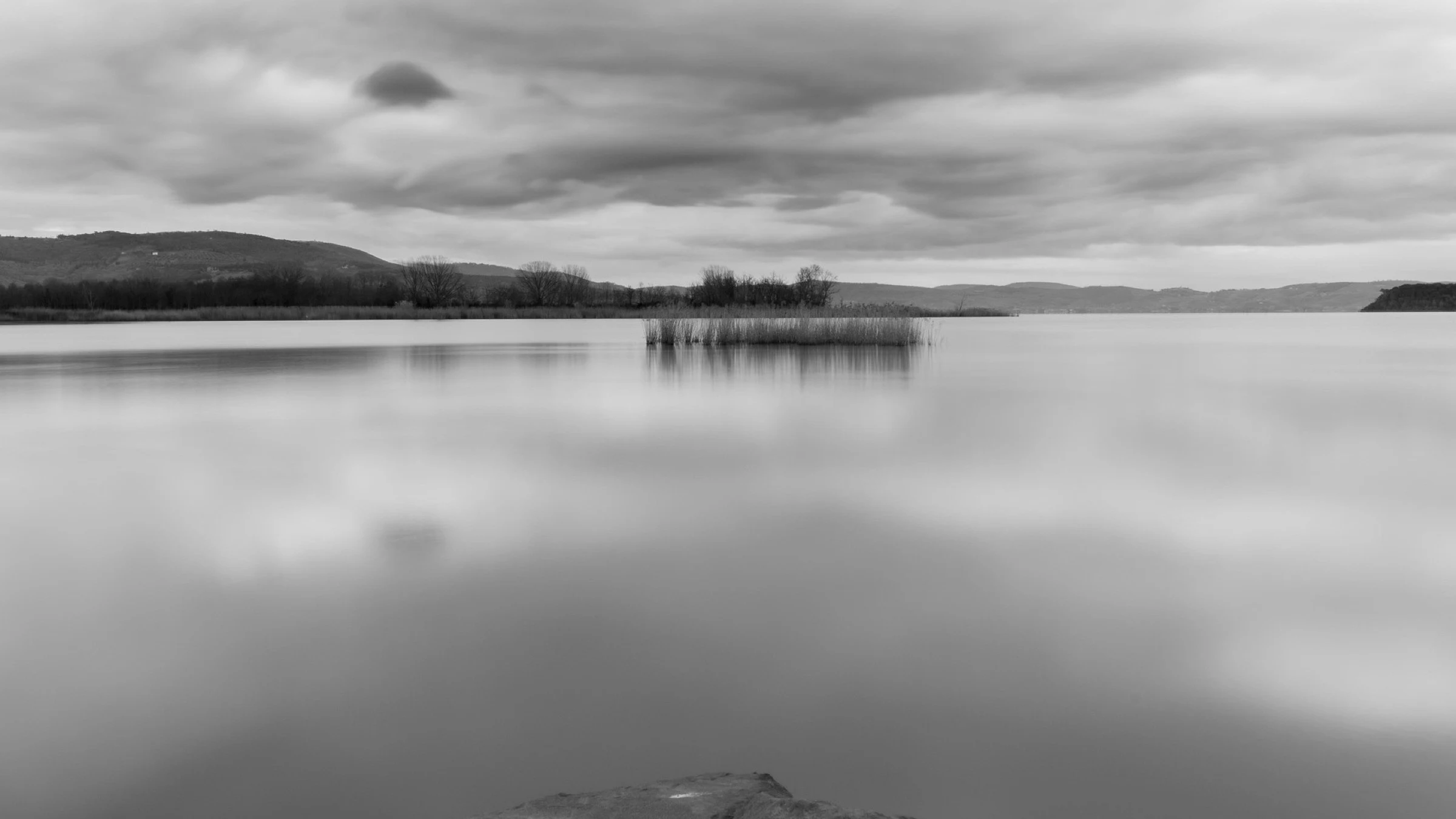 Lake Trasimeno under a cloudy sky with rocks exposed along the water’s edge.