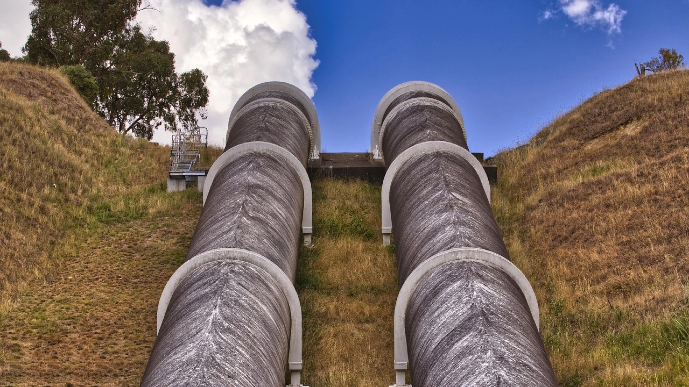 Large water pipes and treatment infrastructure beside a reservoir.