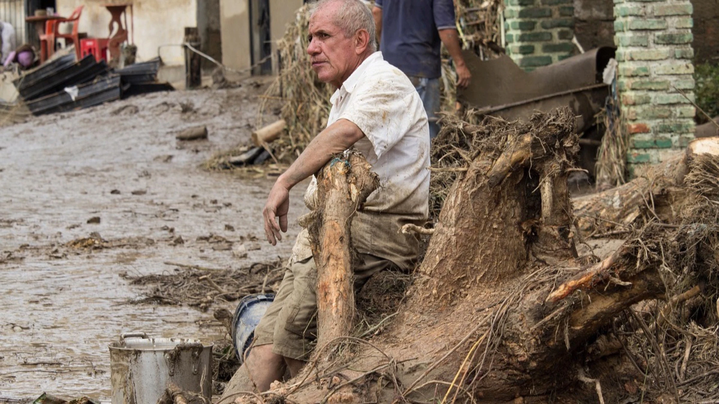 A resident sits among mud and debris left by severe flooding.