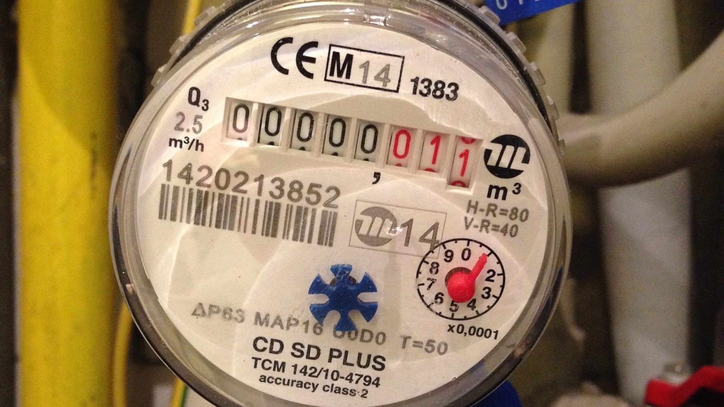Close-up of a mechanical household water meter and connected pipes.