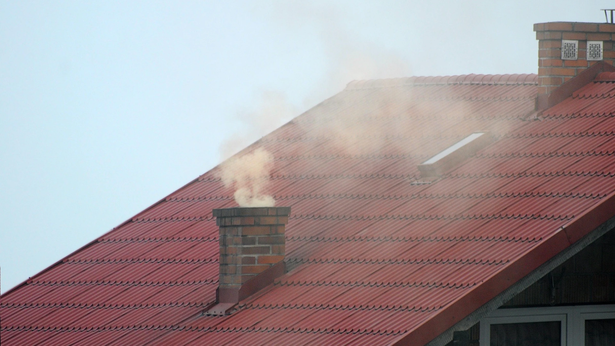 Smoke rising from a chimney above a tiled roof.