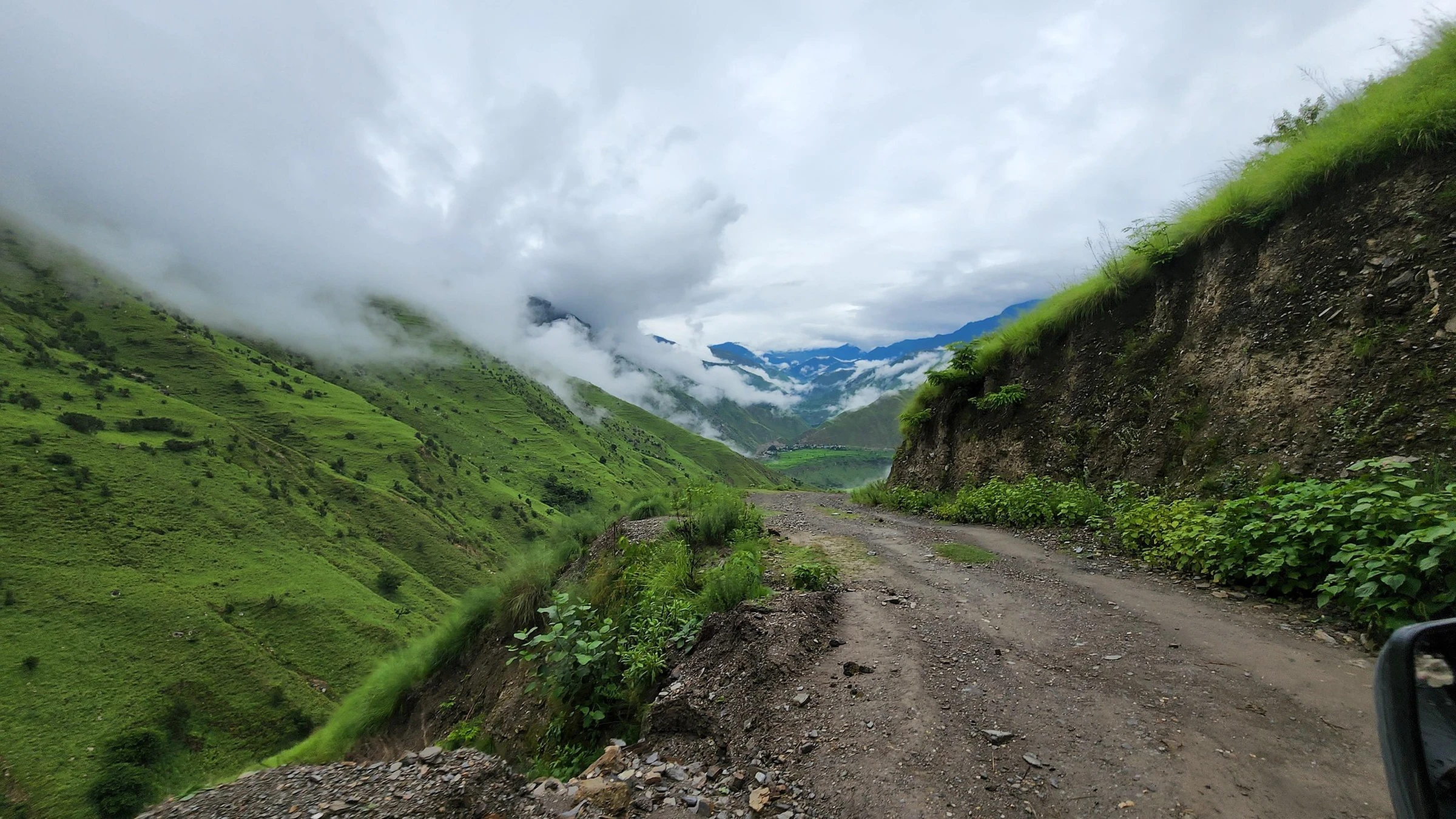 Unpaved road along a green mountain slope under cloud in Nepal.