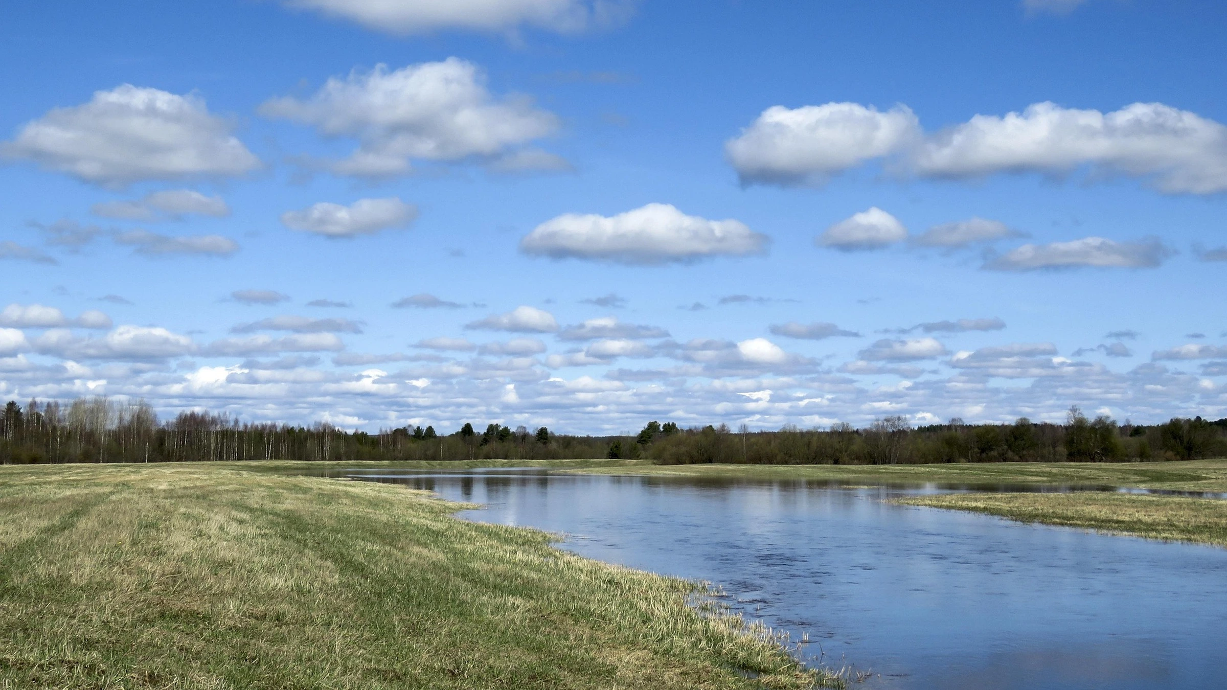River beside a grassy floodplain under a cloudy sky