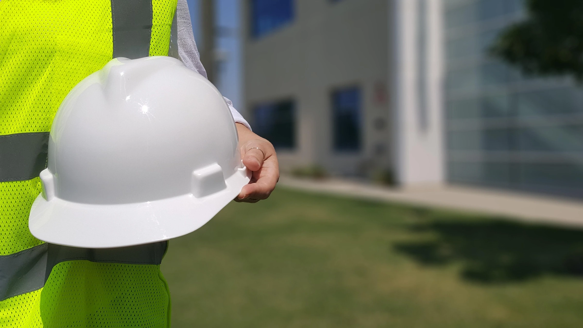 A person in a high-visibility vest holding a white hard hat, with the face outside the frame.