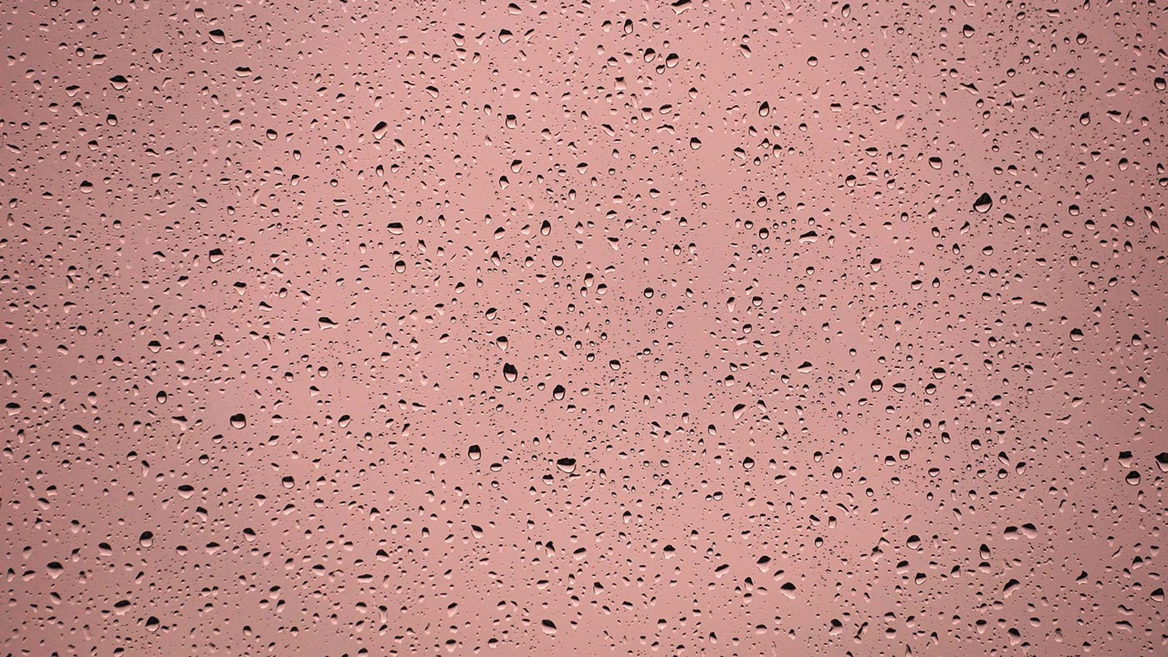 Raindrops across a window against a muted pink background.