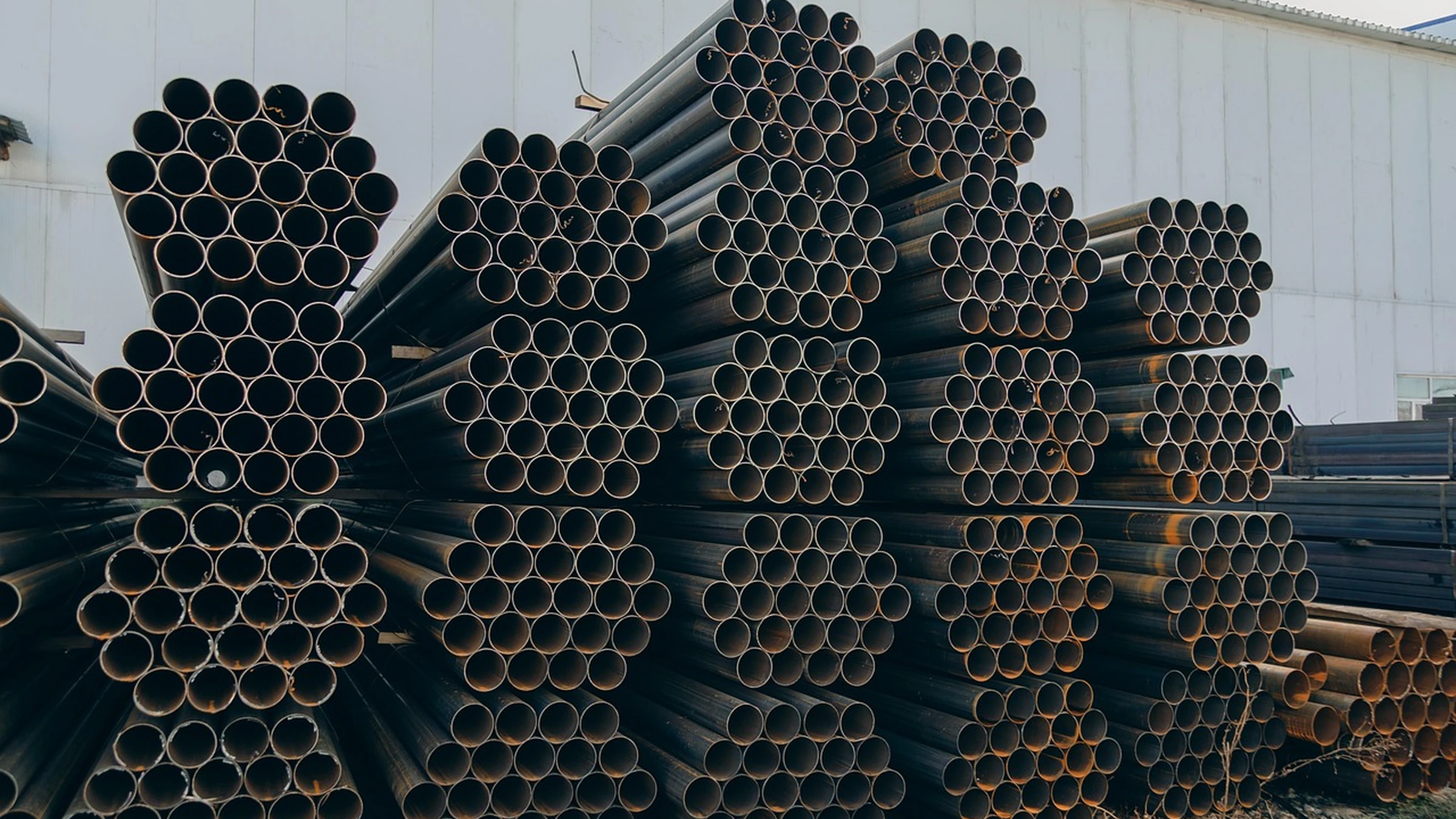 Stacked steel pipes beside an industrial building.