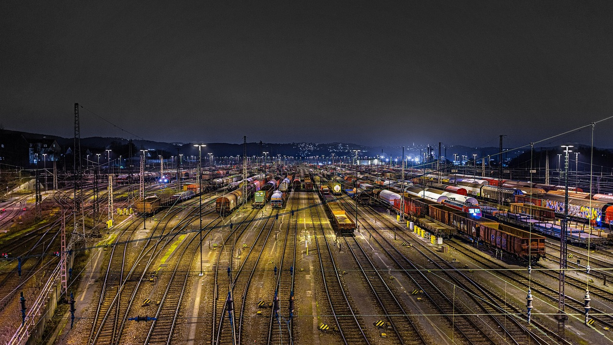 Parallel tracks and freight trains in a railway depot at night.