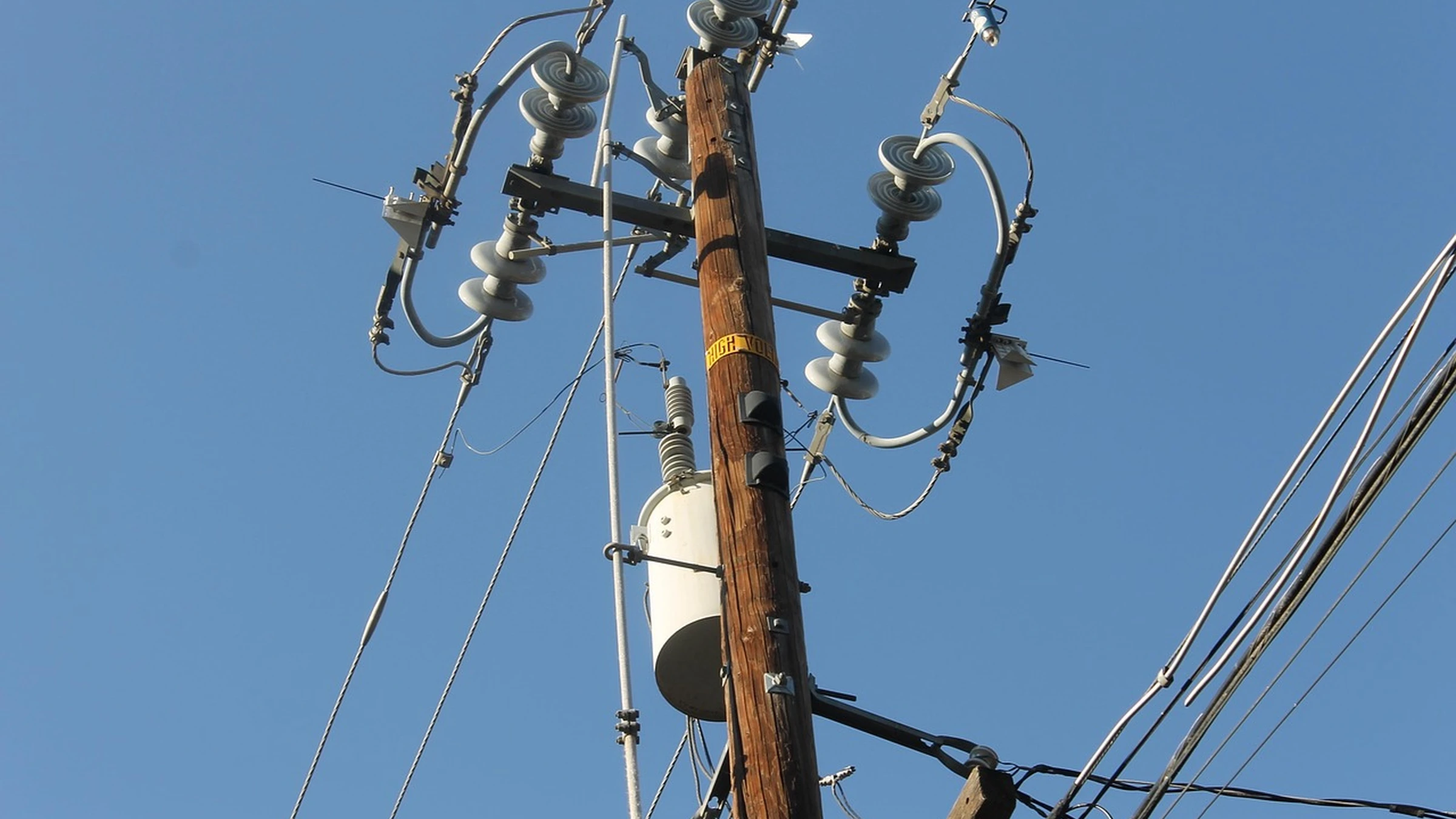 Pole-mounted transformer and overhead electricity wires against blue sky